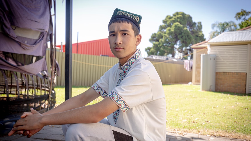 Young Uyghur boy sitting in his backyard in traditional clothes 