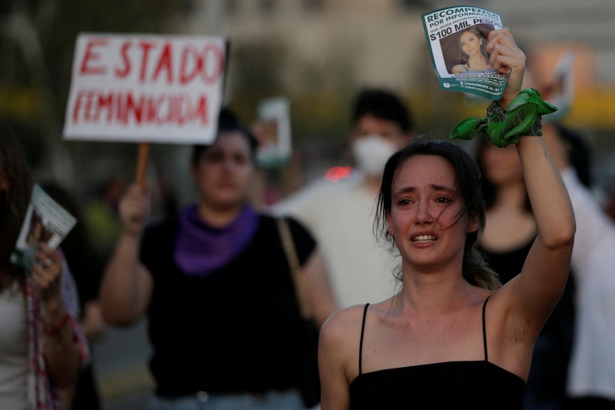 Une jeune femme en robe bustier noire a l'air affligée alors qu'elle lève la photo d'une femme devant un rassemblement