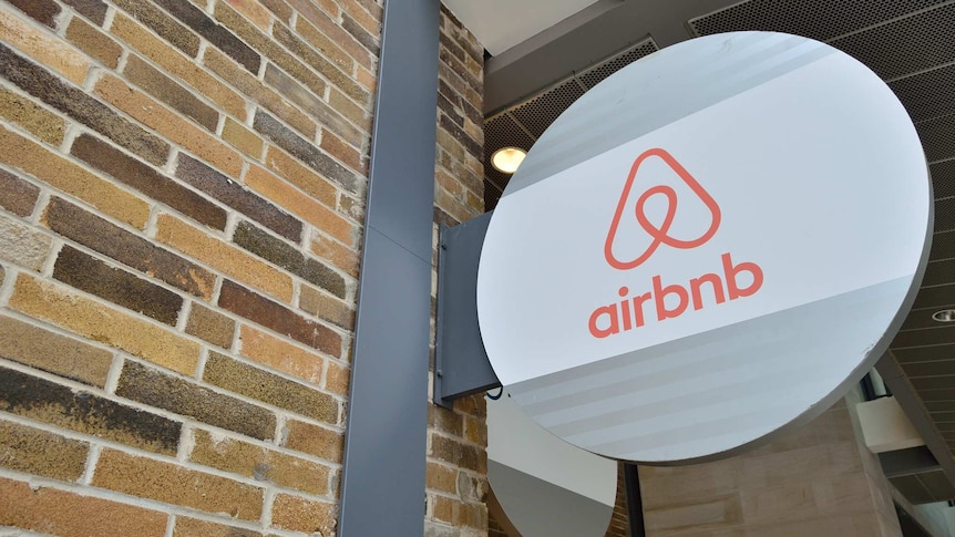 A sign depicting the Airbnb logo juts out from a brick wall.