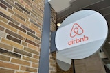 A sign depicting the Airbnb logo juts out from a brick wall.