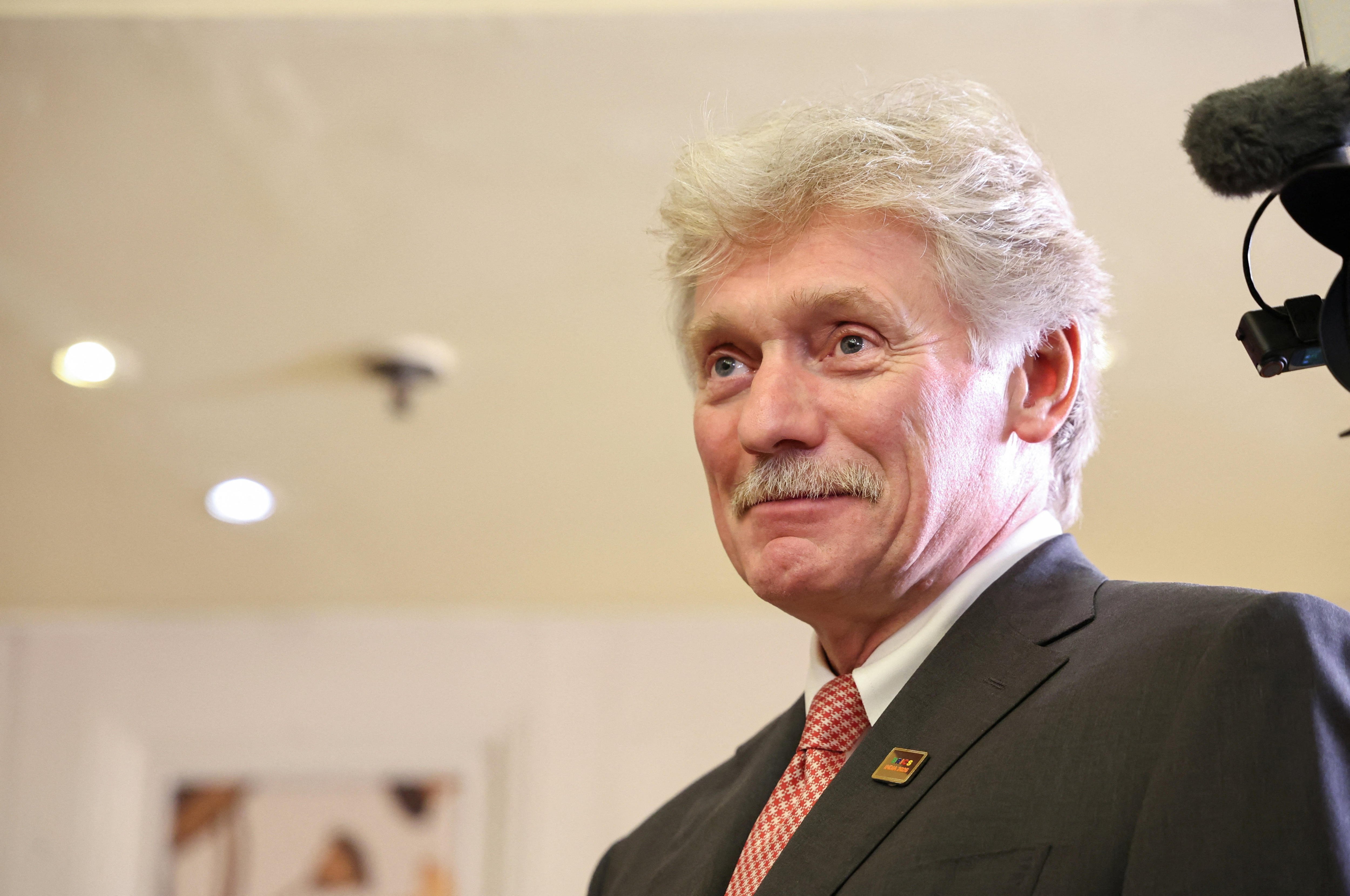 Dmitry Peskov wearing a black suit and red tie, photographed from below.