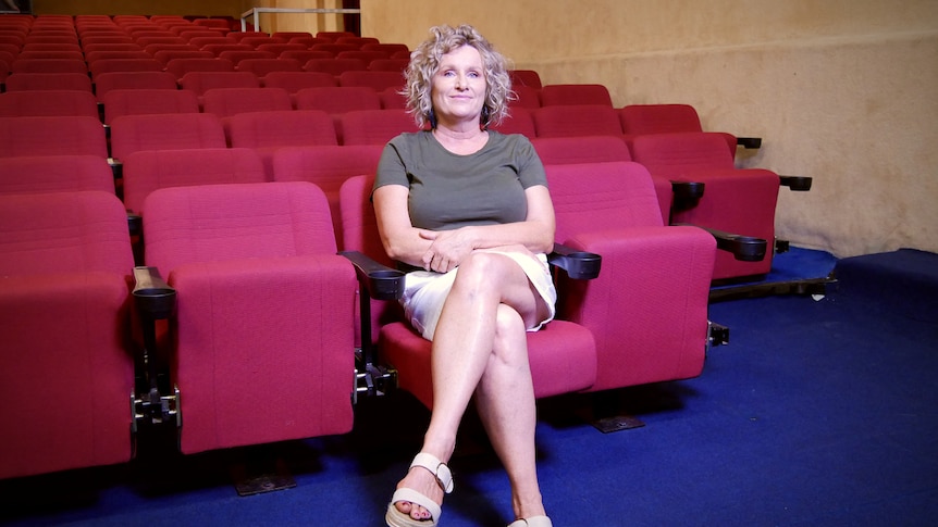 A woman sits alone in the front row of an empty cinema.