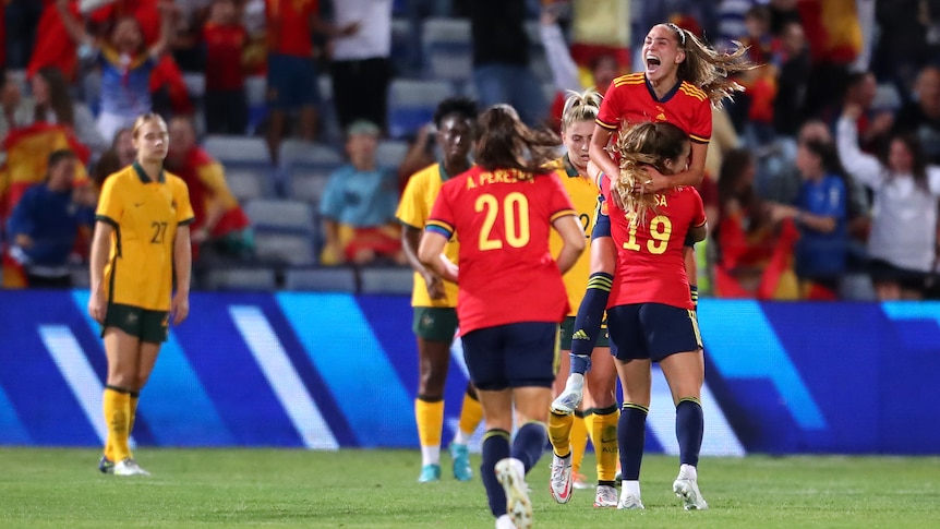 A Spanish goalscorer leaps into her teammate's arms as the Matildas look dejected during a soccer international.