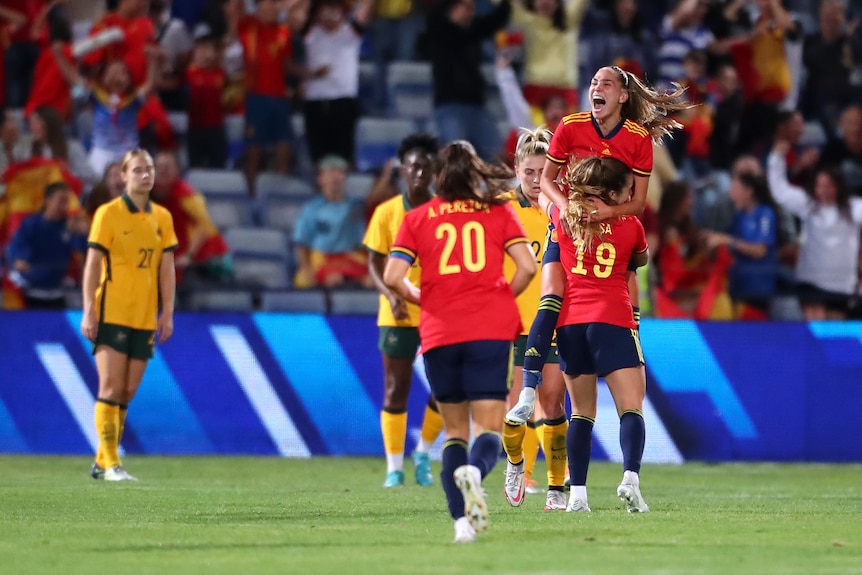 A Spanish goalscorer leaps into her teammate's arms as the Matildas look dejected during a soccer international.