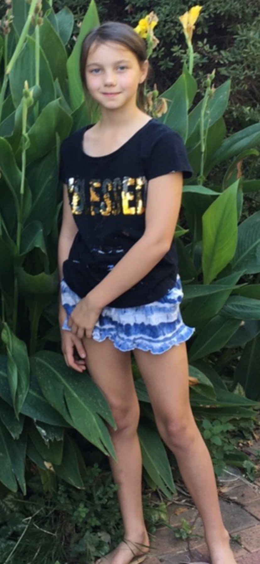 A smiling, dark-haired girl stands in a garden.