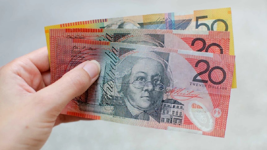 A woman's hand holding up Australian currency, one fifty and two twenty dollar notes.