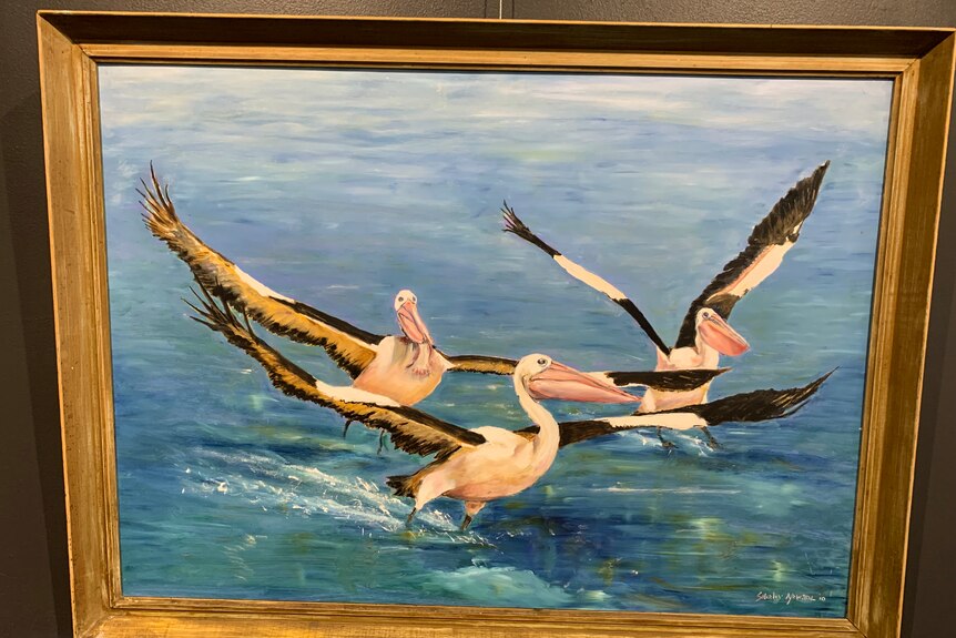 An oil painting of three pelicans taking off on a lake in a golden frame