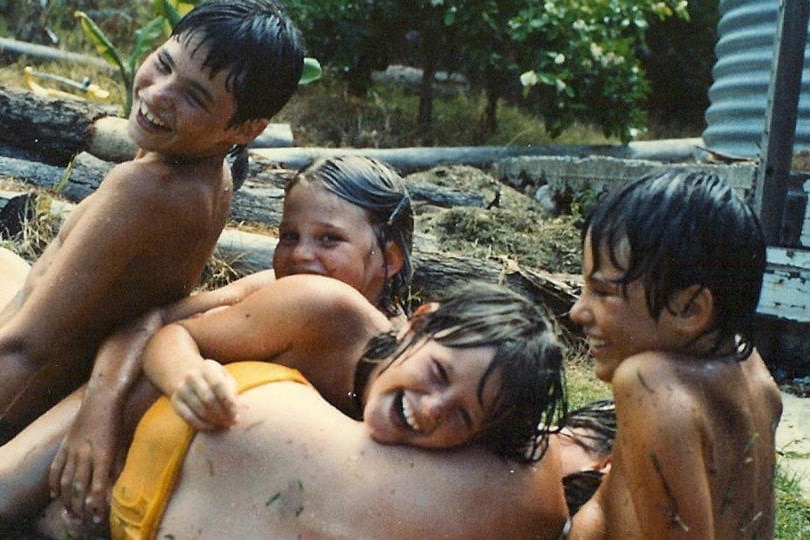 Four children laugh and giggle with wet hair in a backyard