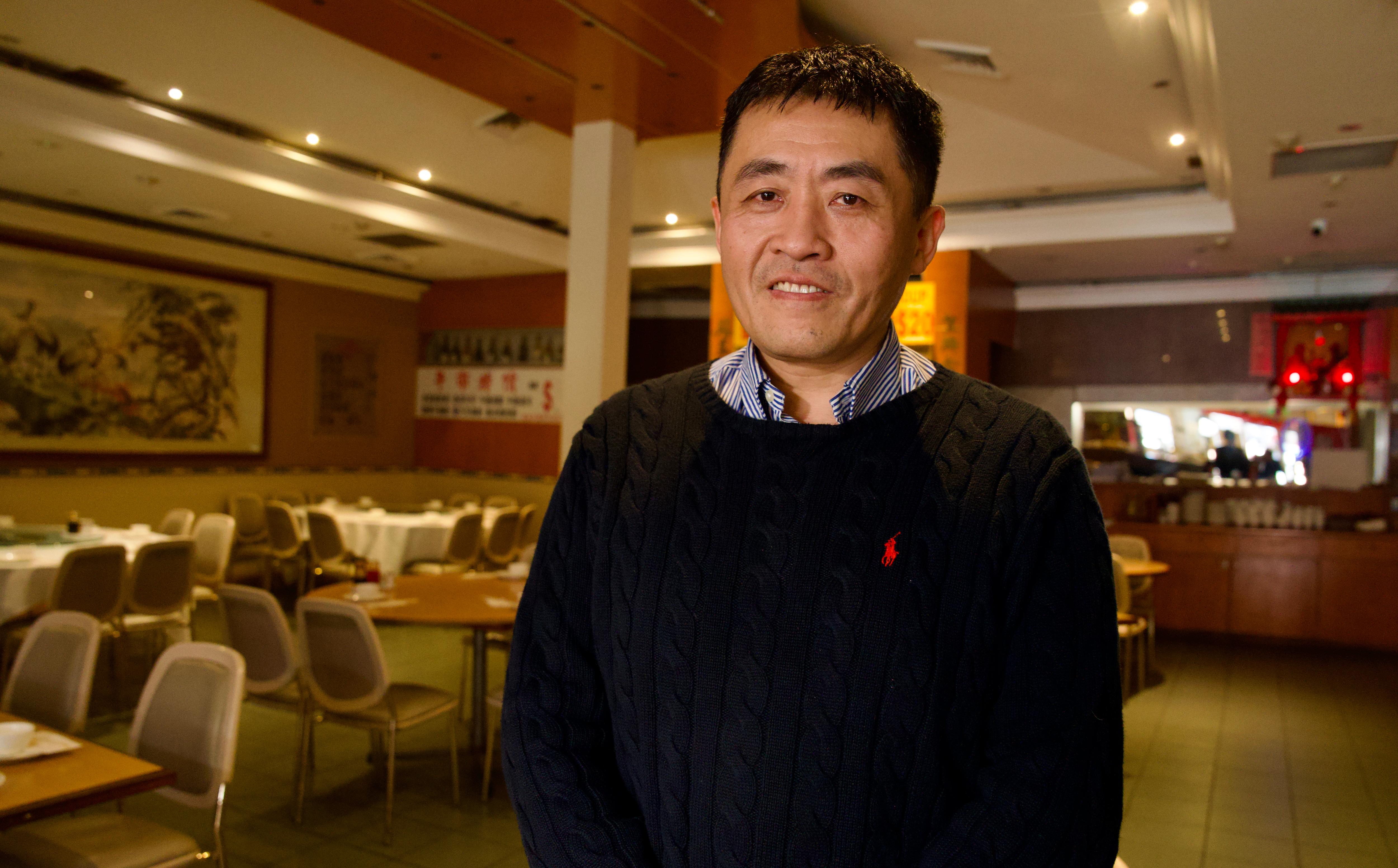 Valentine poses for a photo inside a restaurant, wearing a jumper.