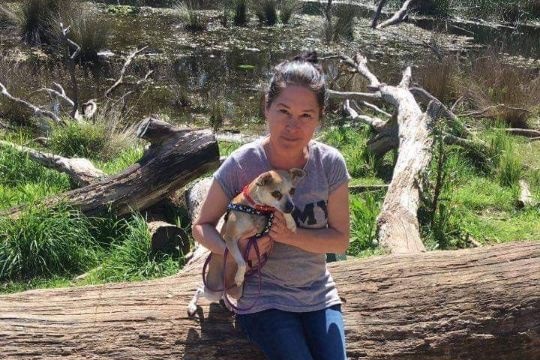 A woman sitting on a log holding a small dog