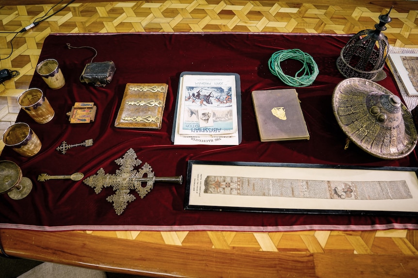 A collection of Ethiopian artefacts including a crown, shield, cups, prayer books and a necklace.