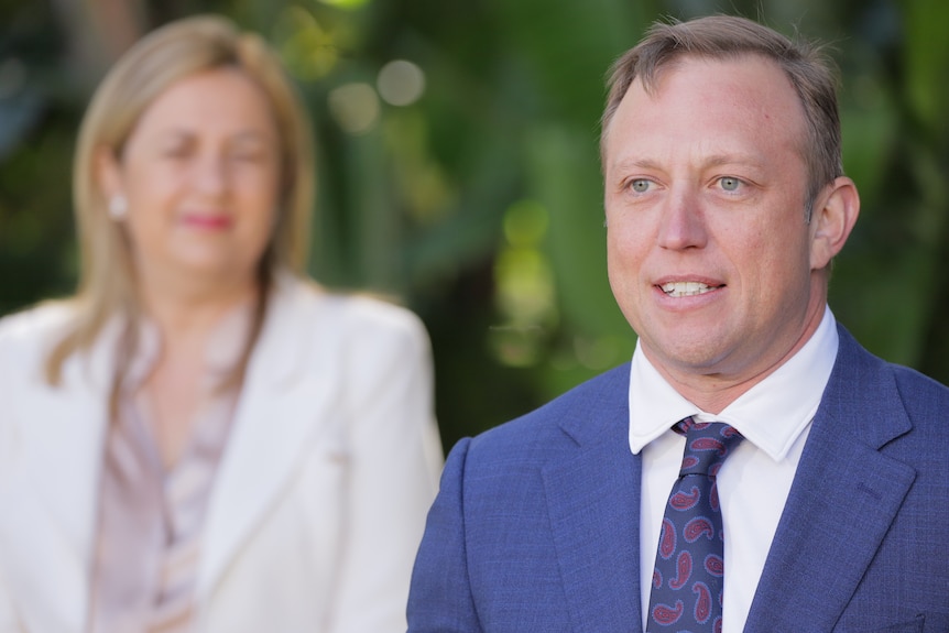 A close-up of Steven Miles speaking with Annastacia Palaszczuk blurred in the background