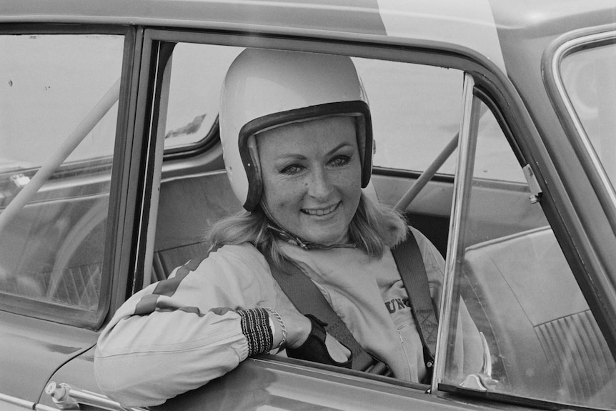 Archival black-and-white photo of a smiling Rosemary Smith, wearing a helmet and sitting in a car, in 1967.