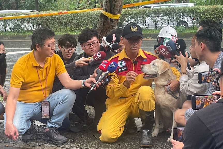 Reporters holding microphones surround a dog and his handler. 
