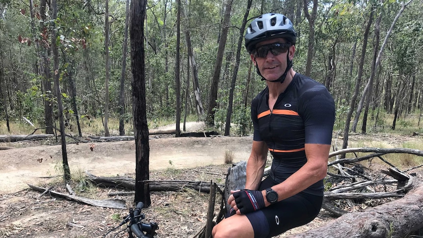 Troy Bayliss sitting on a mountain bike in the forest.