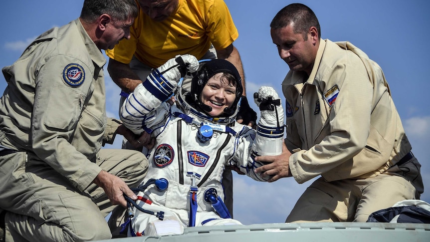 Anne McClain is all smiles as ground staff help her out of the capsule after landing