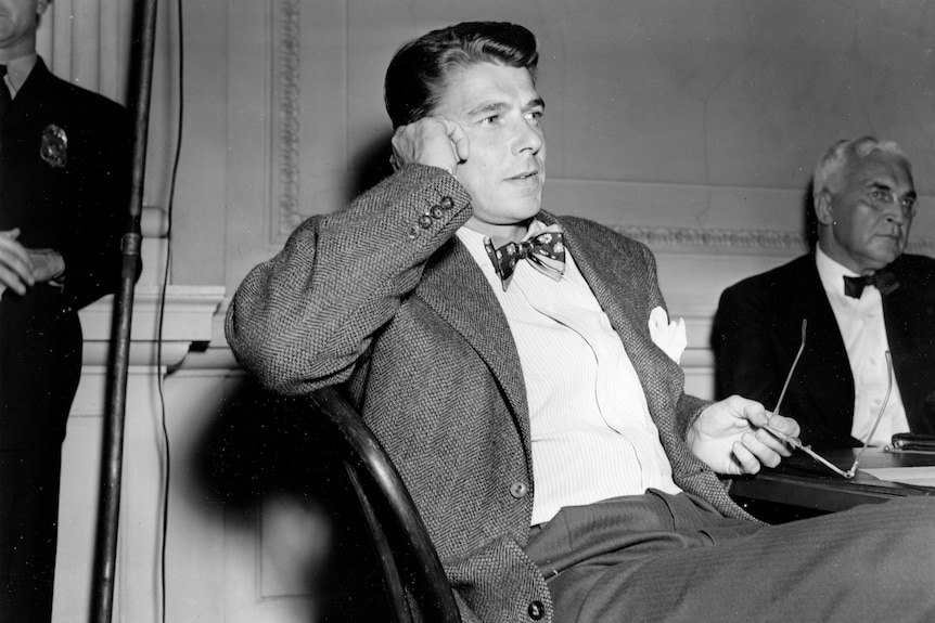 A black and white image of Ronald Reagan reclining in his seat. 