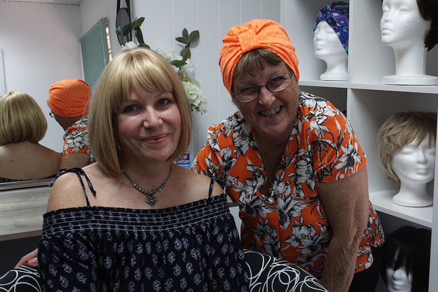 Two ladies smiling side by side wearing bright orange.