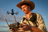 Young cattle grazier holding remote control with drone hovering in background
