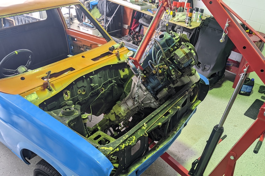 A workshop crane hoists an engine from the front compartment of a Datsun