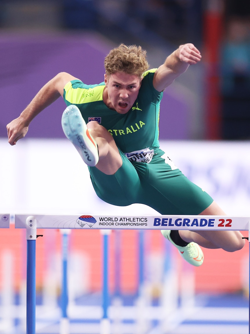 A man wearing green and yellow races in the hurdles