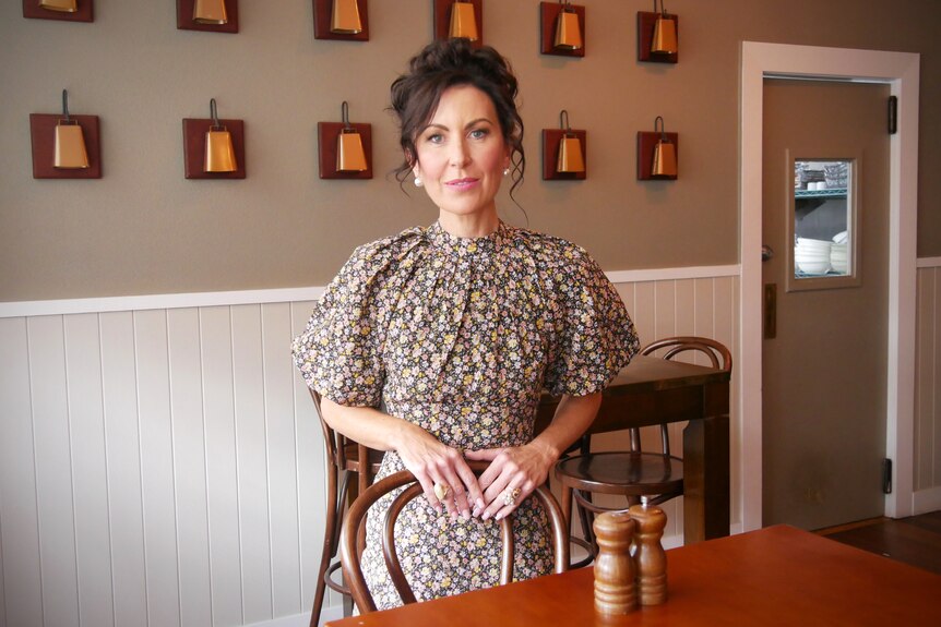 A woman in a floral dress stands behind a pub table.