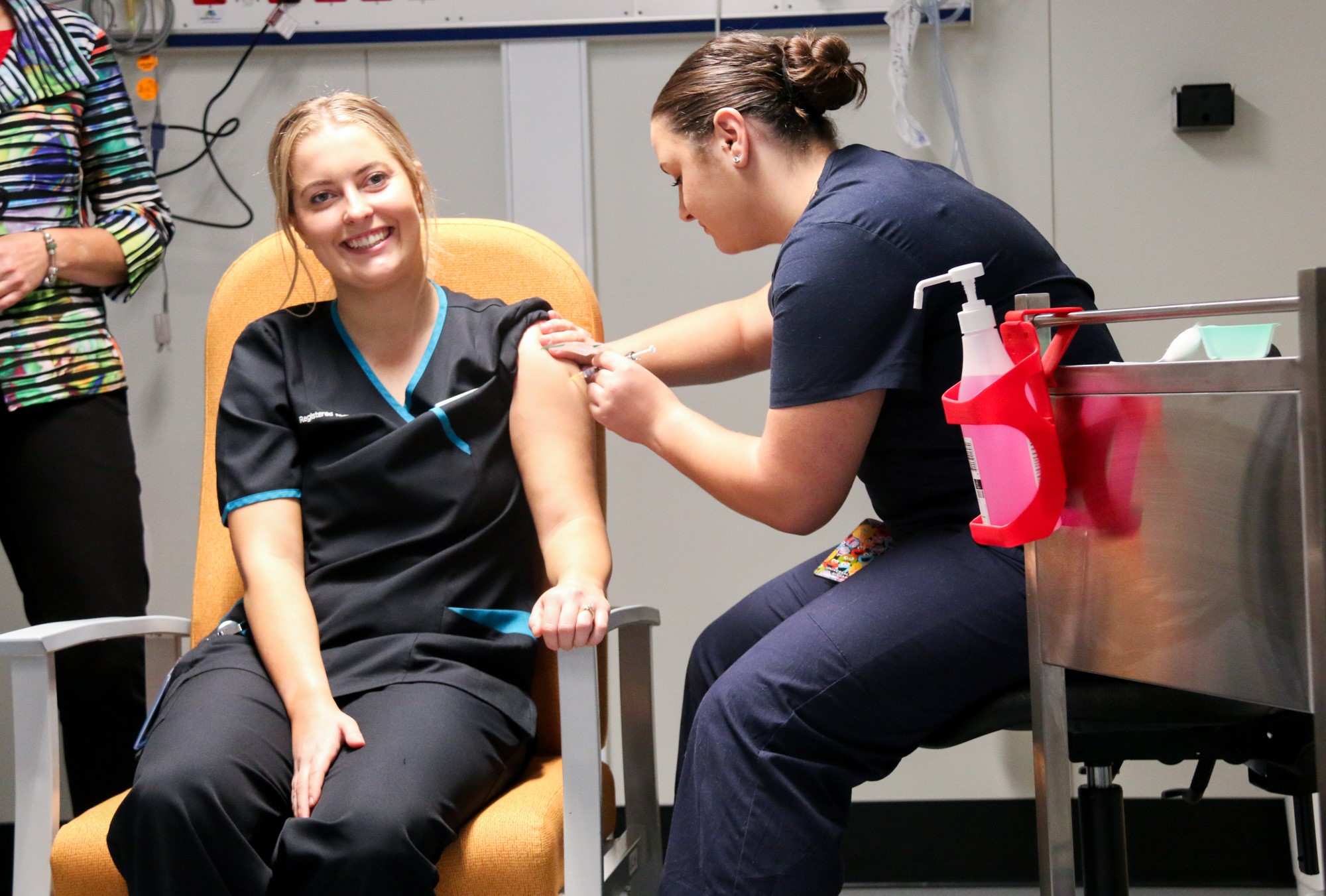 a woman smiling while being jabbed with a needle