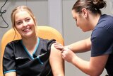 a woman smiling while being jabbed with a needle