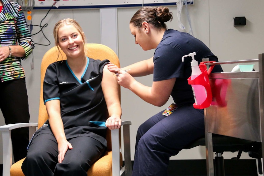 a woman smiling while being jabbed with a needle