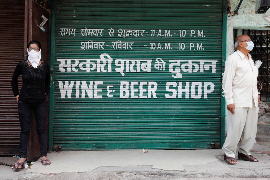 People stnad on either side of a shopfront shutter reading Wine and Beer SHop. 