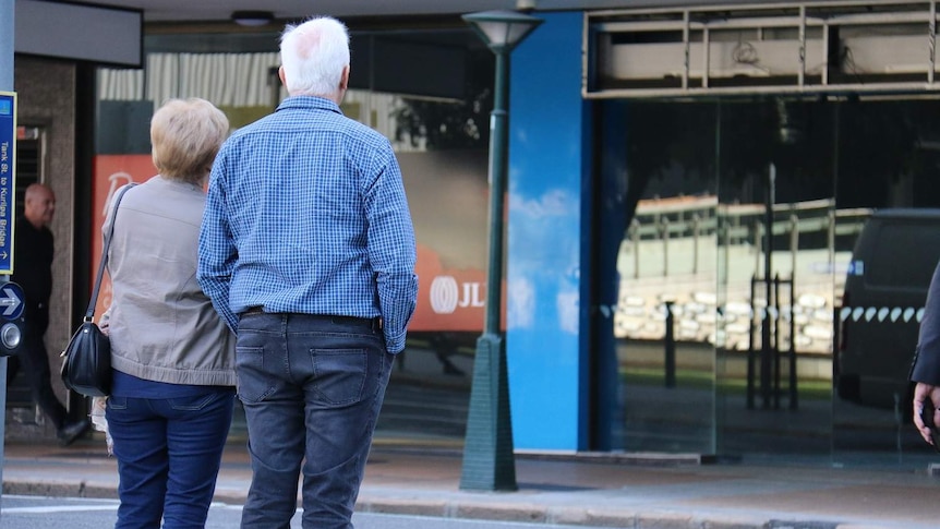 Senior-aged couple standing next to each other while they wait to cross the road in Brisbane's CBD.