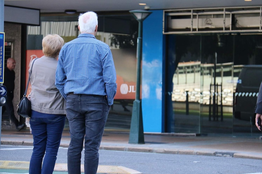 Senior-aged couple standing next to each other while they wait to cross the road in Brisbane's CBD.