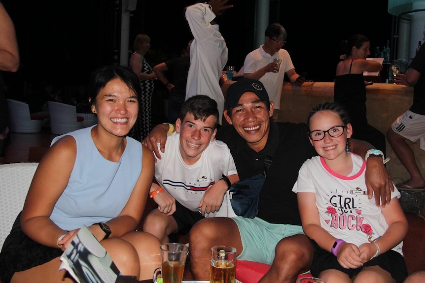 Two children sit with a couple smiling and posing for a photo in a restaurant.