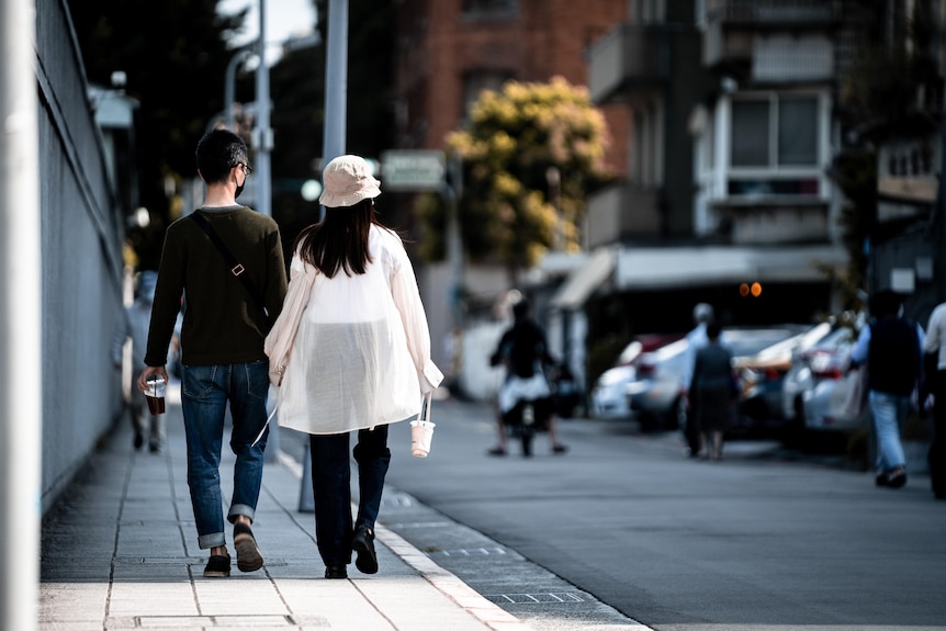 A man and a woman wearing a hat and long white shirt walk down a street.