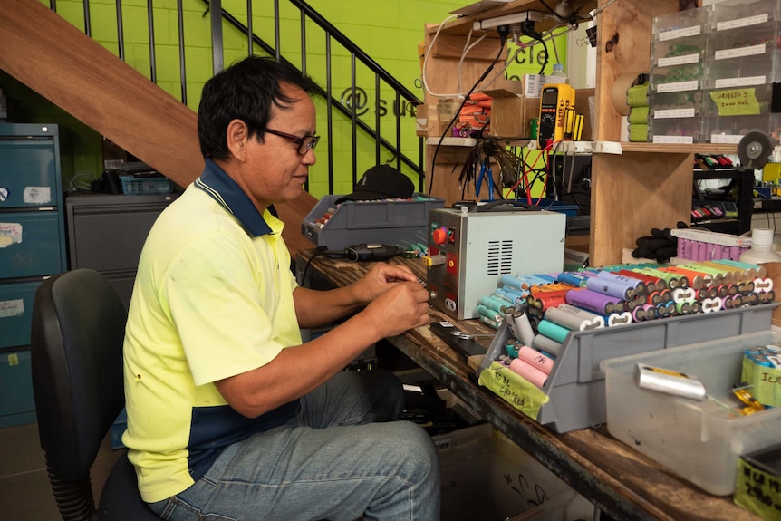 A man sitting at a desk processing colourful batteries.