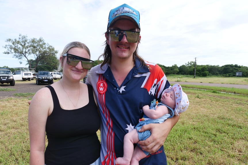 A woman and a man wearing sunglasses while holding a baby.
