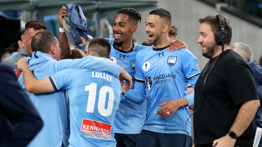 Fabio Gomes and Gabriel Lacerda celebrate winning the Australia Cup in a huddle with Sydney FC teammates.