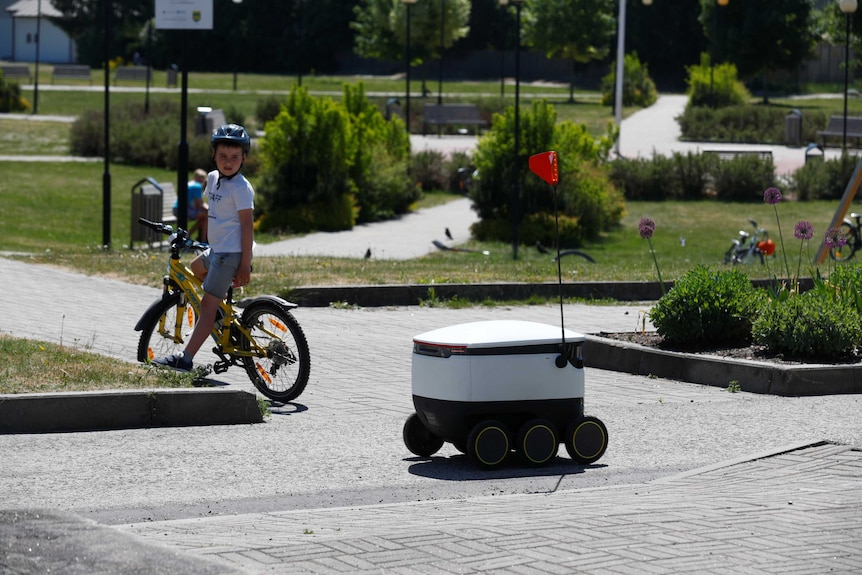 A boy on his bike stops to watch a Starship local delivery robot.