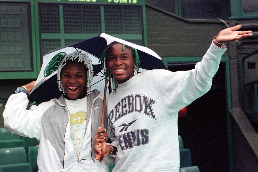 Serena and Venus as teenagers facing the camera and smiling, beads in hair