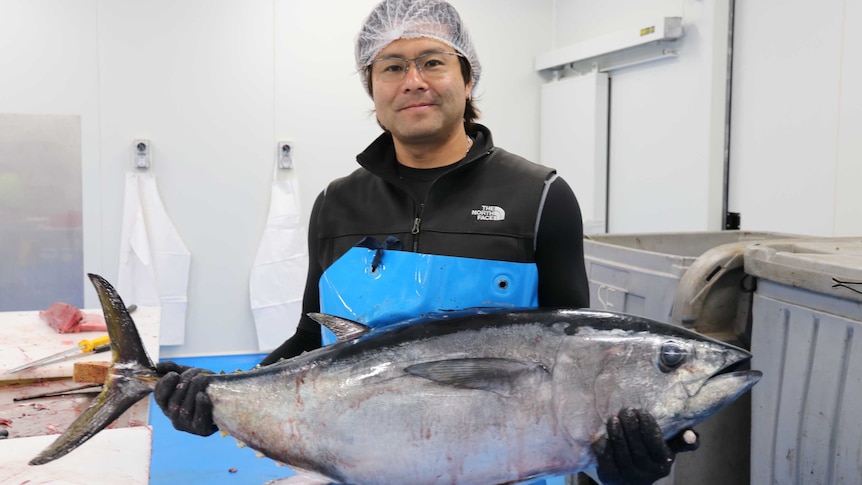 Man holding southern bluefin tuna horizontal to him in factory setting