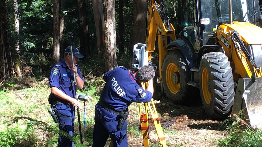 Police officers survey the search area near a digger.