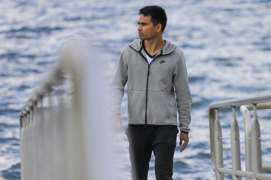 A man in a grey jumper overlooks the water from a pontoon