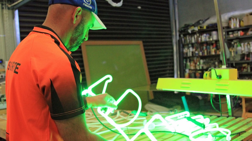 A man in fluoro orange t-shirt holding green neon tubes