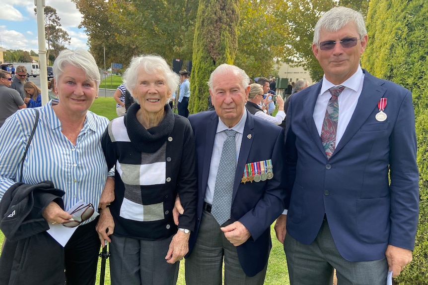 Two women and two men stand together at an Anzac service, both men wearing military badges.
