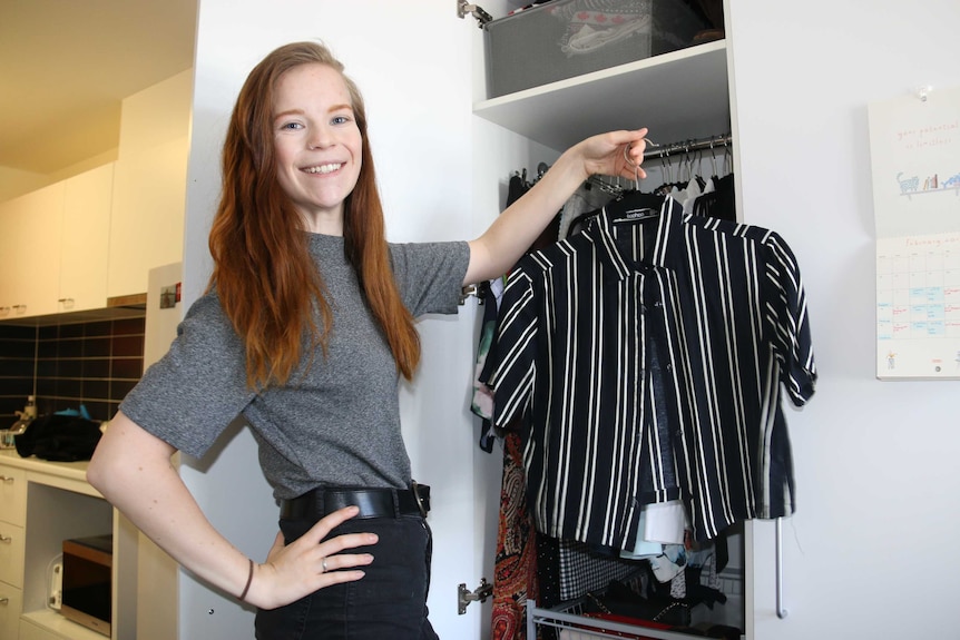 Kaitlyn holds up a striped blouse near her wardrobe.