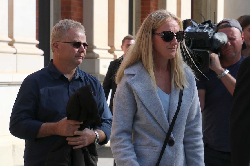 A woman in a long white coat and sunglasses outside court with crowd of other people.