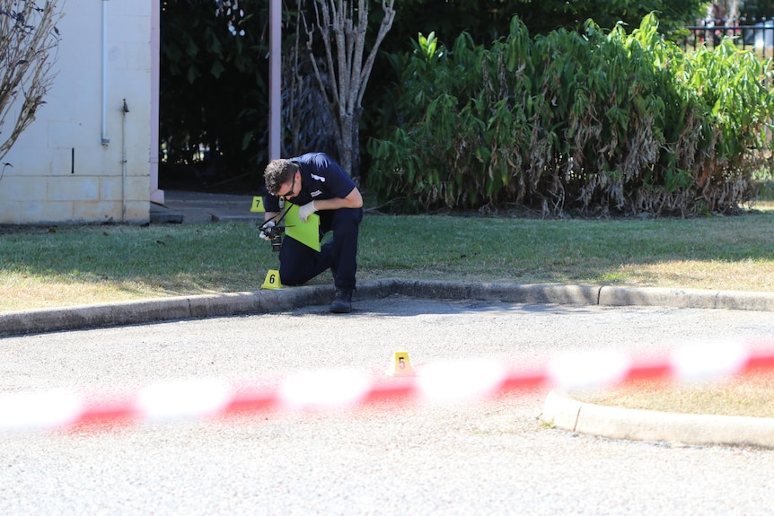 A police officer crouches down at a crime scene while looking at evidence.
