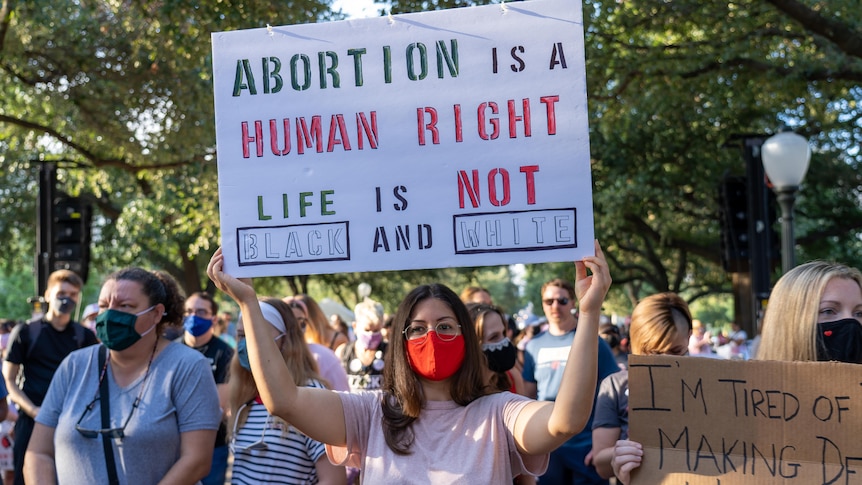 Men and women at a protest. One woman holds a sign that reads: 'Abortion is a human right, life is not black and white.'