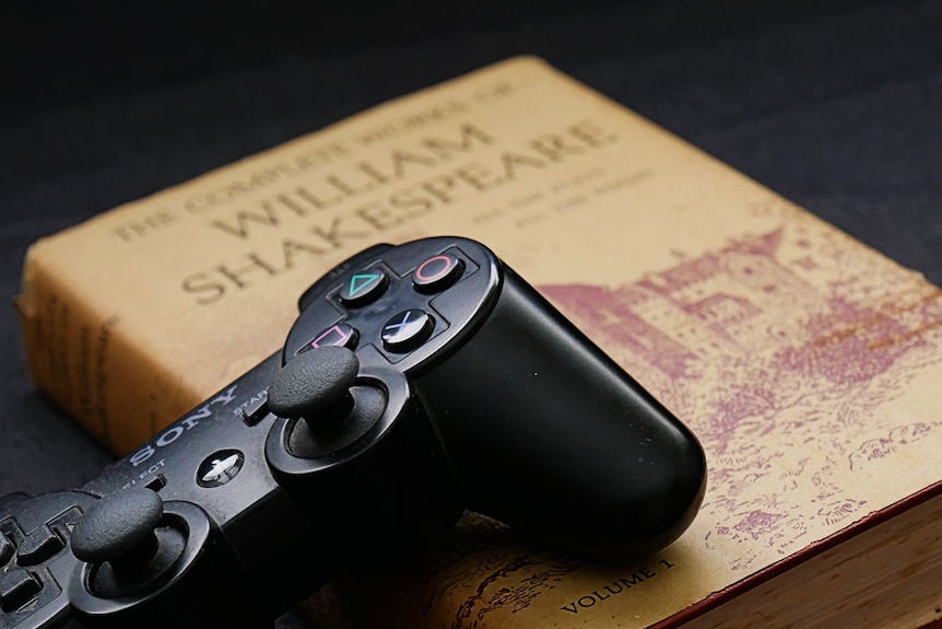 A game controller sits on top of old Shakespeare book