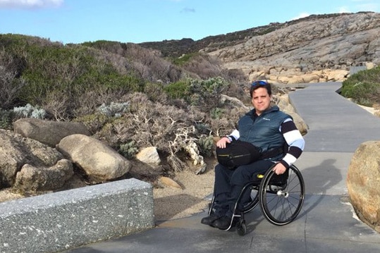 A man in a wheelchair on a path against a rocky backdrop.